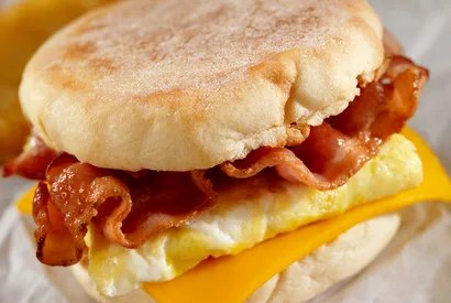 A breakfast sandwich featuring crispy bacon, fluffy egg, and melted American cheese on an English muffin, ideal for foodservice and quick-service restaurant menus.
