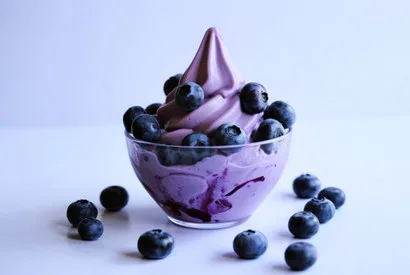 Purple frozen yogurt swirl topped with fresh blueberries in a clear bowl, ideal for food service and dessert distribution.