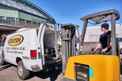 Food service delivery scene with a van, forklift, and bustling logistics at a commercial dock.