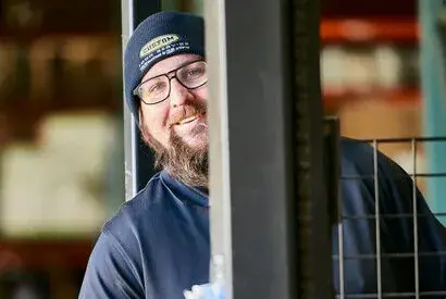 Friendly man in beanie smiles in a warehouse setting, promoting teamwork and approachability.