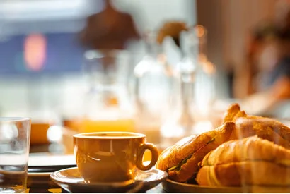 Elegant breakfast table setting featuring croissants, coffee service, and glassware in a hospitality dining environment, ideal for food service operations.