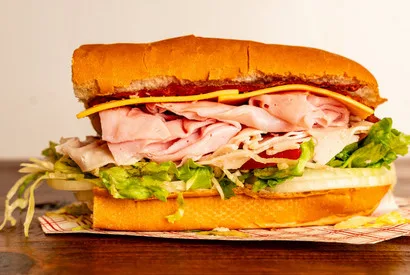 Gourmet deli sandwich featuring sliced premium meats, fresh lettuce, and cheese on toasted bread roll for wholesale food distribution and foodservice supply.