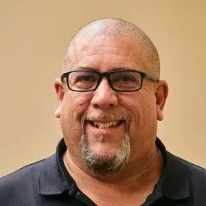 Friendly middle-aged man with glasses and a warm smile in a casual black polo shirt.