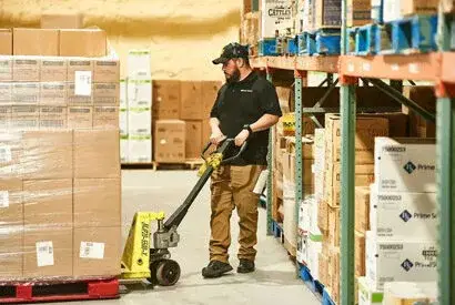 Warehouse worker using a pallet jack to efficiently manage inventory in a well-organized space.